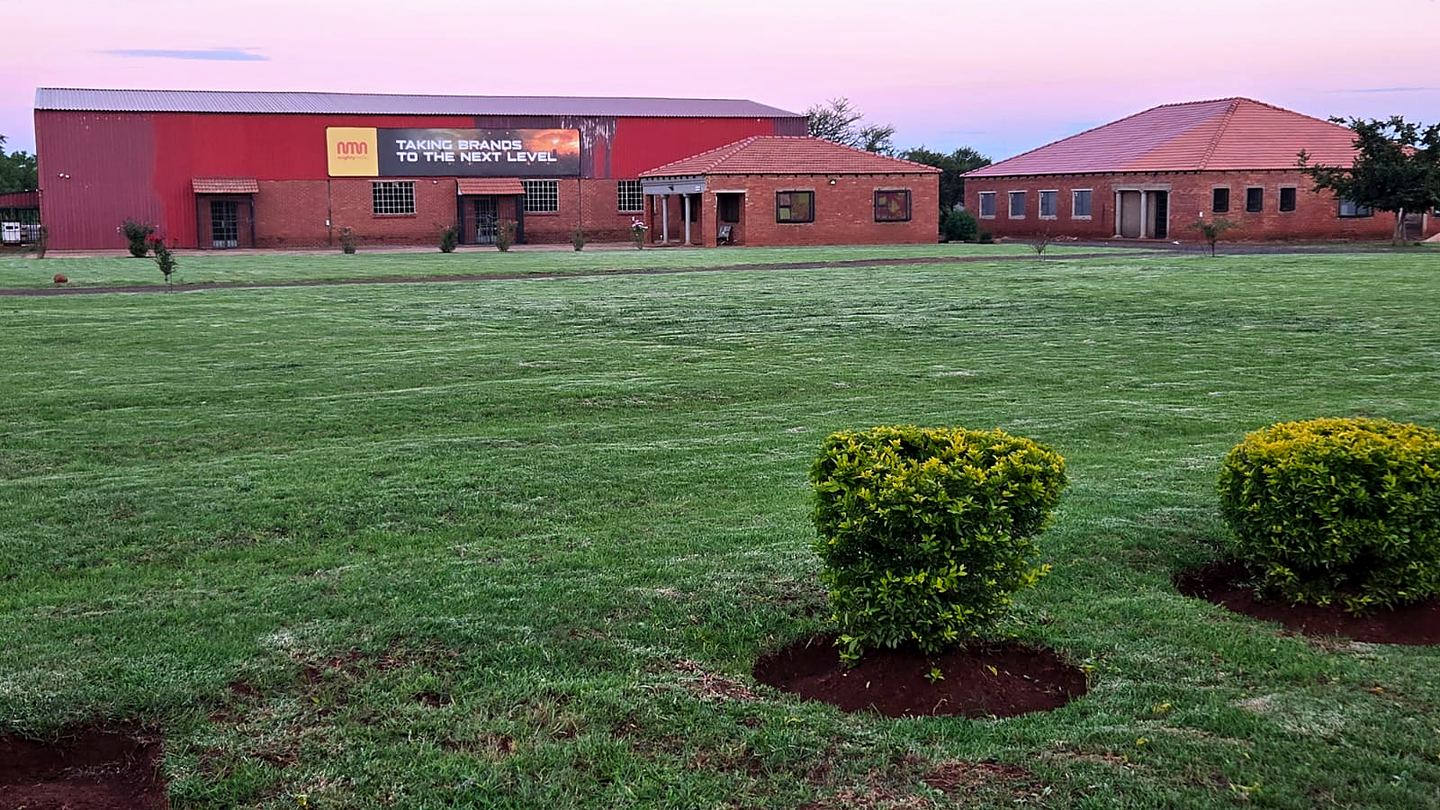 The Mighty Media premises in Roodeplaat at dusk: red workshop building with yellow signage and lawn